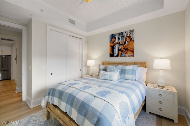 bedroom featuring a raised ceiling, light wood-type flooring, stainless steel refrigerator, and a closet