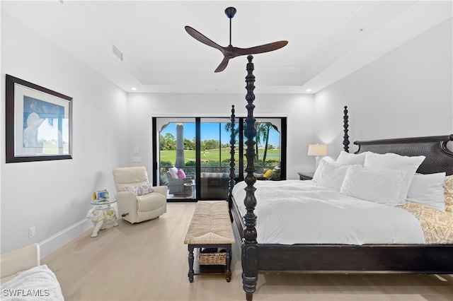 bedroom featuring hardwood / wood-style floors, ceiling fan, a raised ceiling, and access to exterior