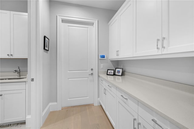 bar with light hardwood / wood-style floors, white cabinetry, and sink