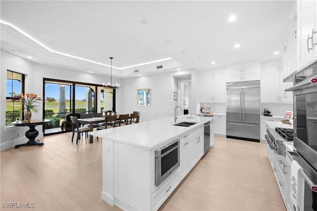 kitchen with white cabinets, appliances with stainless steel finishes, a center island with sink, and a tray ceiling