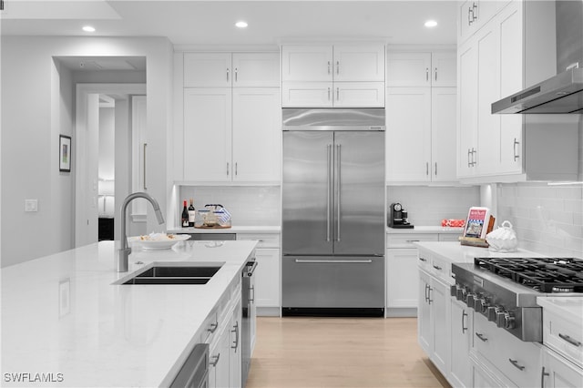 kitchen with wall chimney range hood, sink, decorative backsplash, white cabinetry, and stainless steel appliances