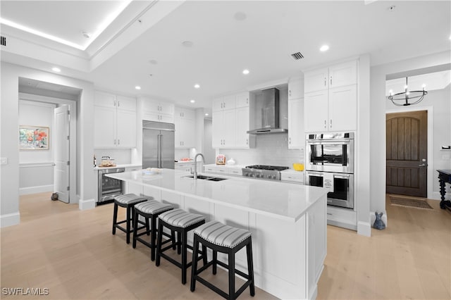 kitchen featuring a large island, wall chimney exhaust hood, sink, and appliances with stainless steel finishes