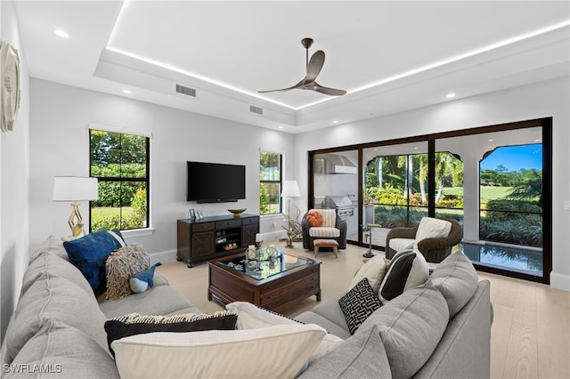 living room with light hardwood / wood-style floors, a wealth of natural light, a tray ceiling, and ceiling fan