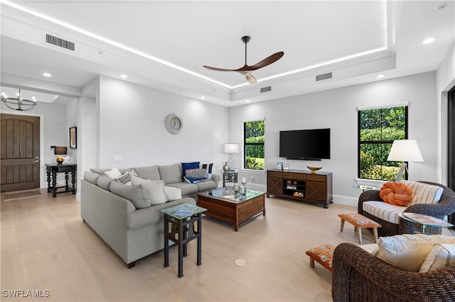 living room featuring a raised ceiling, plenty of natural light, light hardwood / wood-style floors, and ceiling fan with notable chandelier