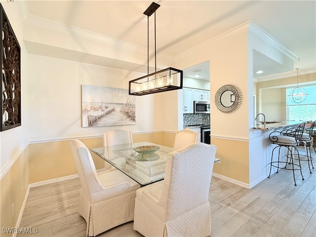 dining room with a notable chandelier, sink, light wood-type flooring, and crown molding