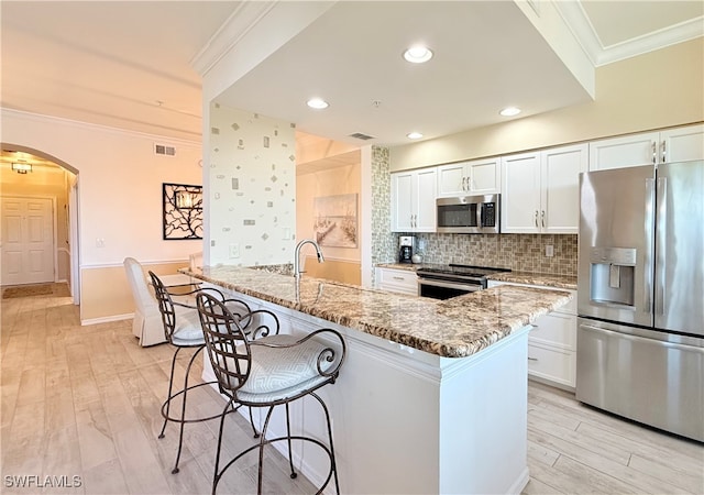 kitchen featuring light stone countertops, white cabinets, light wood-type flooring, and appliances with stainless steel finishes