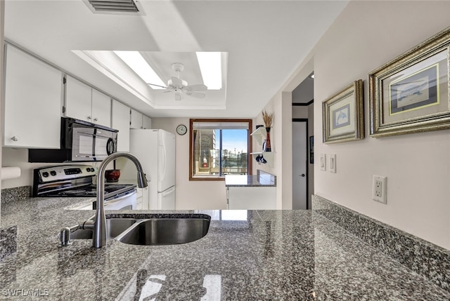 kitchen featuring a raised ceiling, stainless steel electric stove, ceiling fan, white refrigerator, and white cabinetry