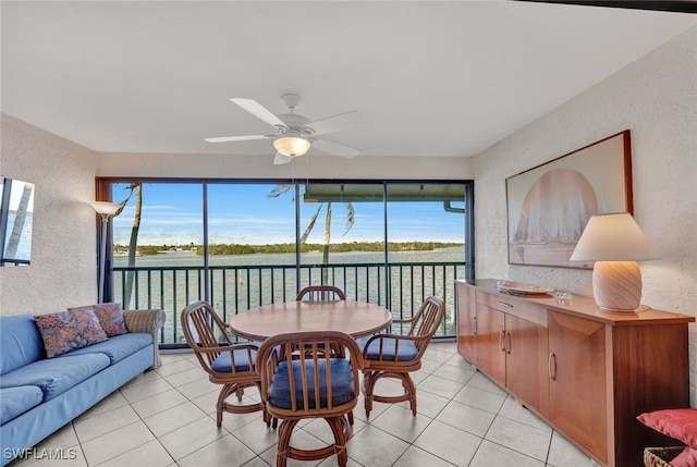 tiled dining room featuring ceiling fan and a water view