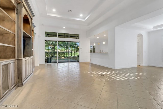 unfurnished living room featuring baseboards, arched walkways, a tray ceiling, recessed lighting, and light tile patterned flooring