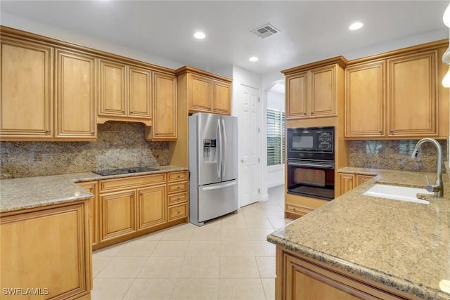 kitchen with light stone counters, light tile patterned flooring, black appliances, arched walkways, and a sink