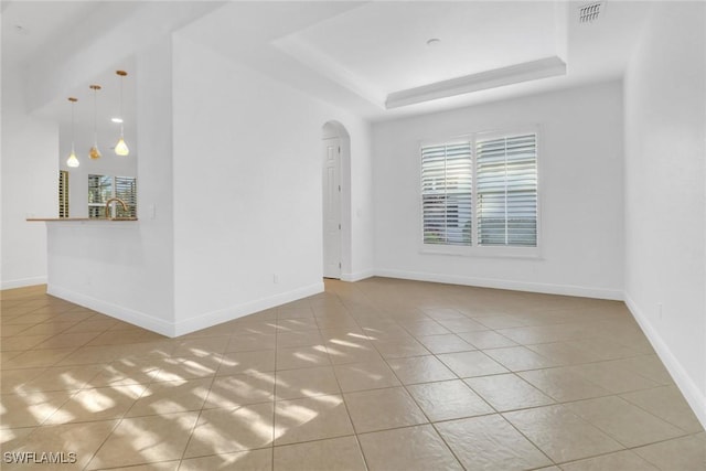 unfurnished room with baseboards, tile patterned floors, visible vents, a tray ceiling, and arched walkways