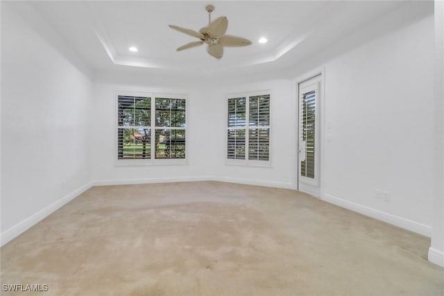 unfurnished room featuring a tray ceiling, light colored carpet, baseboards, and a ceiling fan
