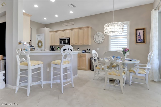 kitchen featuring kitchen peninsula, light brown cabinetry, a notable chandelier, a breakfast bar area, and light tile patterned flooring