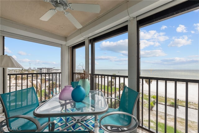 sunroom / solarium with ceiling fan, a water view, and a beach view