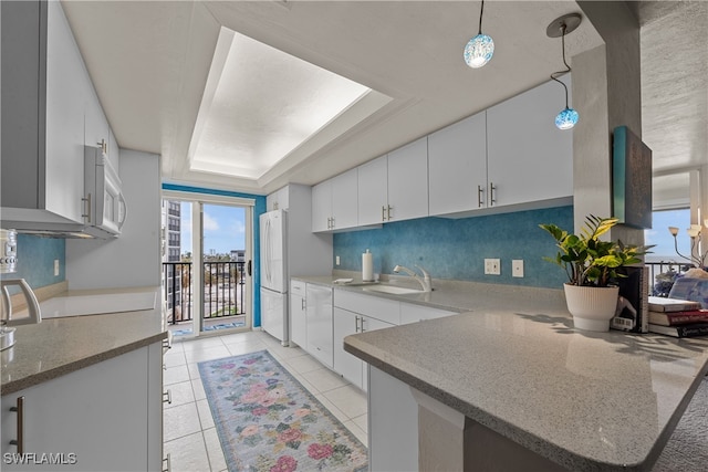 kitchen featuring white appliances, a raised ceiling, sink, hanging light fixtures, and white cabinetry