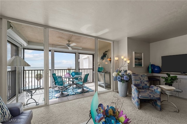 living room featuring light carpet, a wall of windows, a water view, and ceiling fan