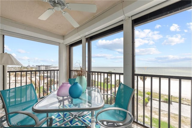 sunroom / solarium featuring a water view, ceiling fan, and a view of the beach