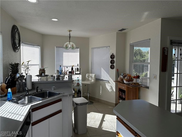 kitchen featuring pendant lighting, sink, a textured ceiling, light tile patterned flooring, and white cabinetry