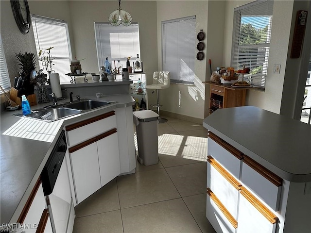 kitchen with tile patterned floors, sink, decorative light fixtures, dishwasher, and white cabinetry