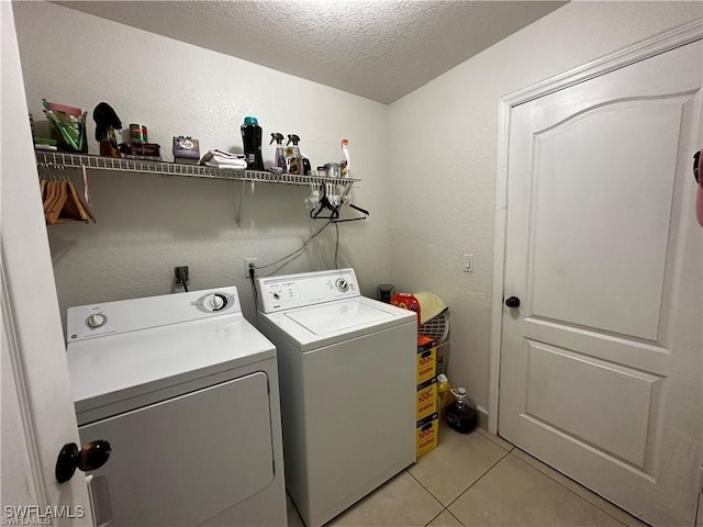 clothes washing area with light tile patterned floors, washer and dryer, and a textured ceiling