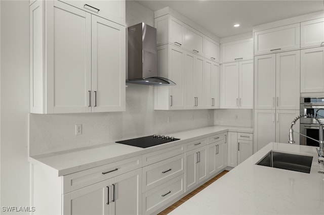 kitchen with sink, stainless steel double oven, wall chimney range hood, black electric cooktop, and white cabinets