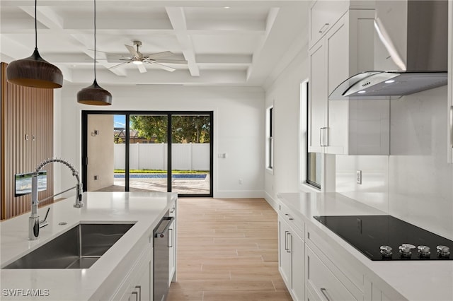 kitchen featuring black electric stovetop, light countertops, white cabinetry, a sink, and wall chimney range hood