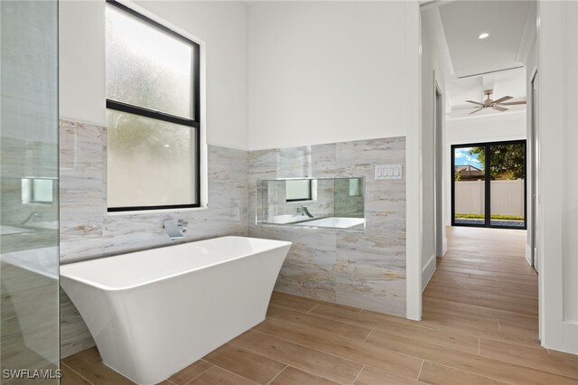 bathroom with ceiling fan, a bathtub, wood-type flooring, and tile walls