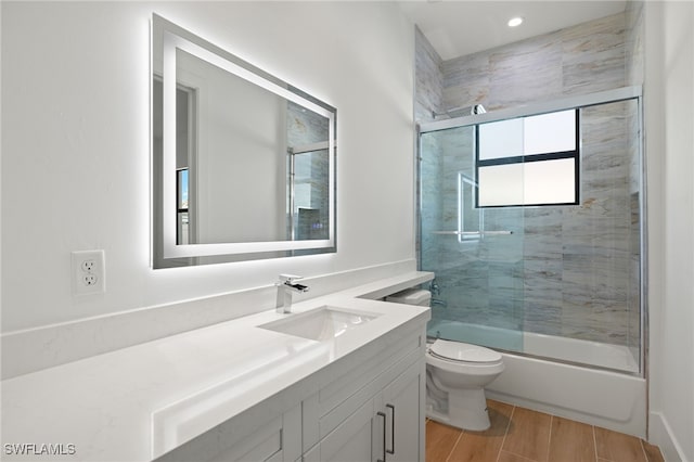 full bath with wood tiled floor, shower / bath combination with glass door, vanity, and toilet