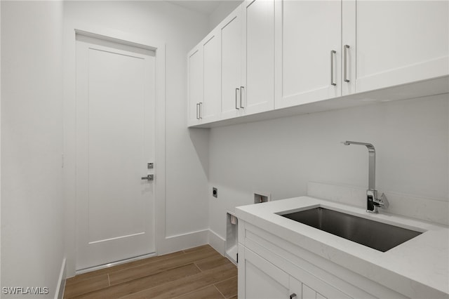 washroom with cabinet space, a sink, electric dryer hookup, wood finished floors, and baseboards