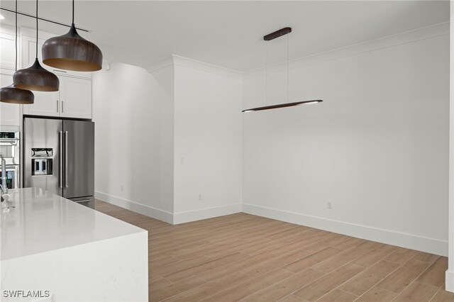 kitchen with appliances with stainless steel finishes, light hardwood / wood-style floors, white cabinetry, and hanging light fixtures