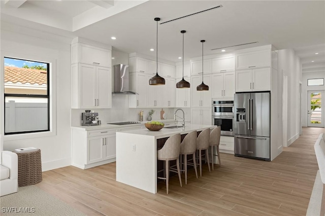 kitchen with light countertops, appliances with stainless steel finishes, wall chimney exhaust hood, and white cabinets