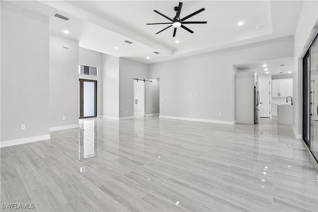 unfurnished living room featuring a raised ceiling, ceiling fan, and sink