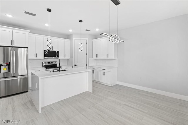 kitchen with appliances with stainless steel finishes, sink, pendant lighting, white cabinets, and an island with sink