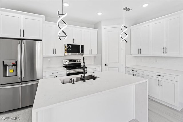 kitchen with appliances with stainless steel finishes, decorative light fixtures, and white cabinetry