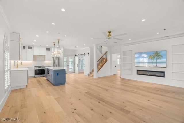 kitchen with white cabinetry, stainless steel appliances, hanging light fixtures, a barn door, and light wood-type flooring