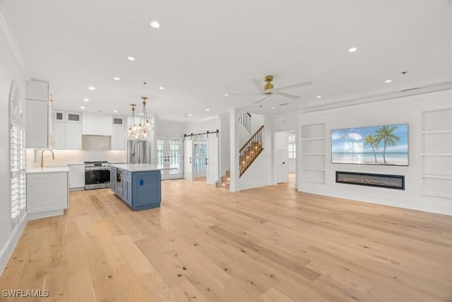 kitchen with open floor plan, stainless steel appliances, a glass covered fireplace, white cabinetry, and light countertops