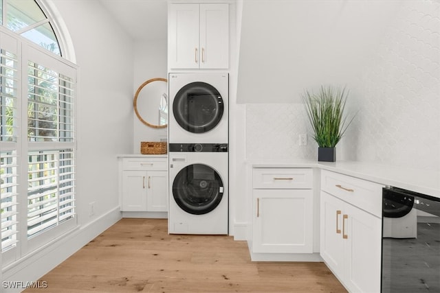 washroom with cabinets, stacked washing maching and dryer, and light hardwood / wood-style flooring