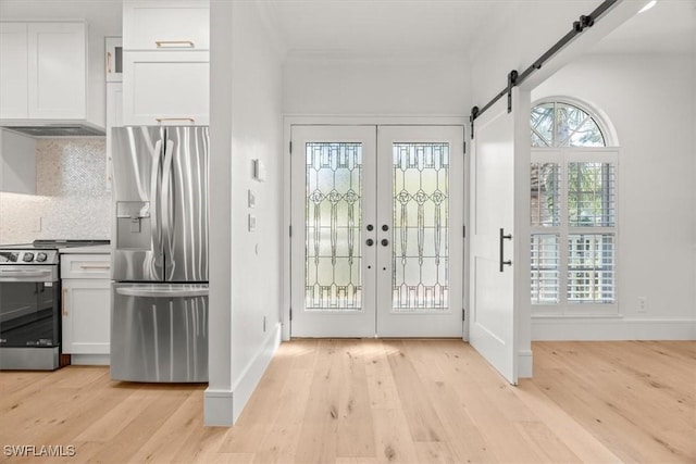 foyer entrance featuring light wood-style flooring, baseboards, a barn door, and french doors