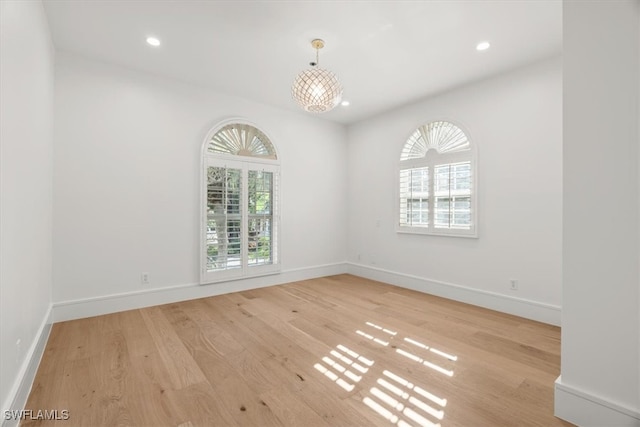 spare room featuring a notable chandelier and light wood-type flooring