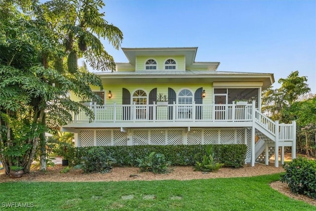 coastal home featuring stairs, a front yard, and a sunroom