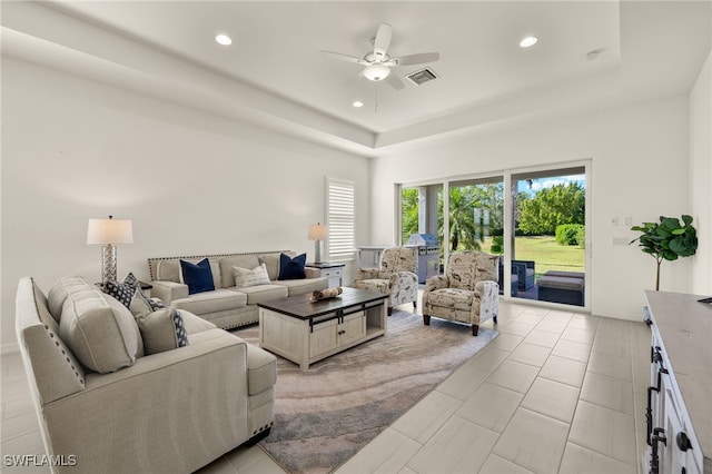 living room with ceiling fan, light tile patterned floors, and a tray ceiling