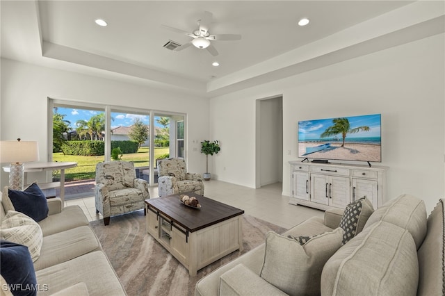 living room with ceiling fan, light tile patterned floors, and a tray ceiling