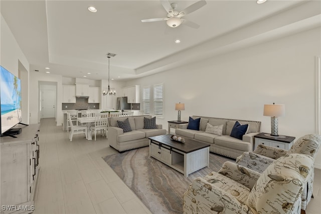 living room with ceiling fan with notable chandelier and a tray ceiling