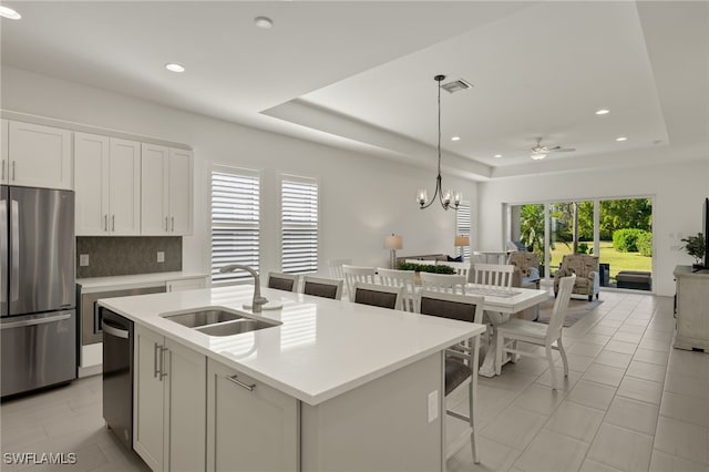 kitchen featuring a raised ceiling, stainless steel appliances, white cabinetry, and a center island with sink