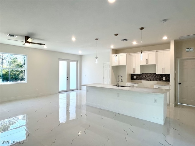 kitchen featuring a large island with sink, sink, decorative backsplash, decorative light fixtures, and white cabinetry