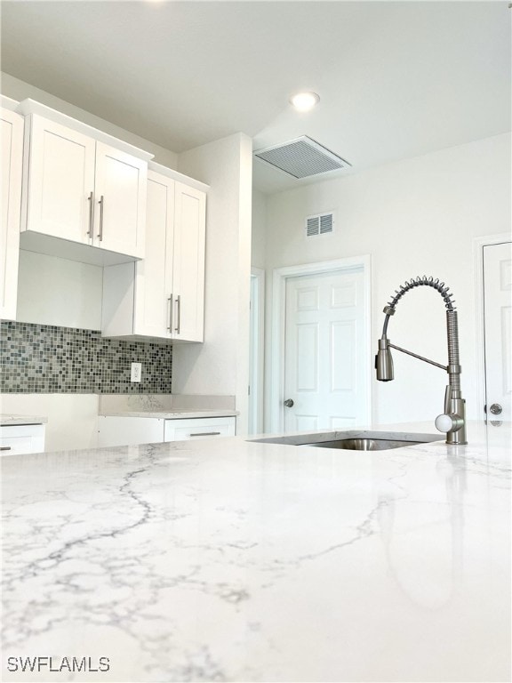 kitchen with light stone countertops, tasteful backsplash, white cabinetry, and sink