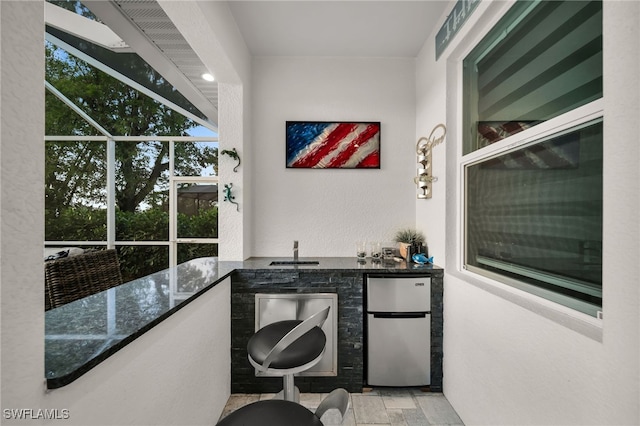 interior space featuring stainless steel fridge, sink, a wealth of natural light, and dark stone counters