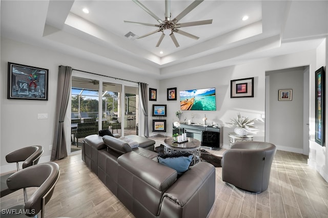 living room featuring bar area, ceiling fan, light hardwood / wood-style floors, and a tray ceiling