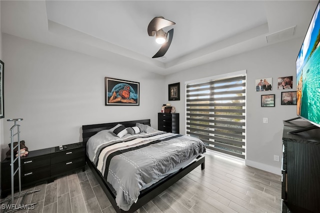 bedroom featuring a raised ceiling, ceiling fan, and light wood-type flooring