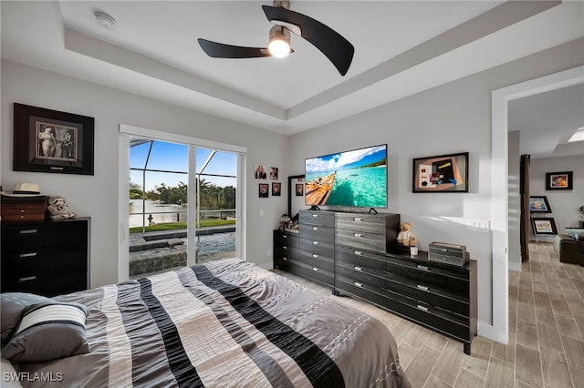 bedroom featuring ceiling fan, light hardwood / wood-style floors, access to outside, and a tray ceiling